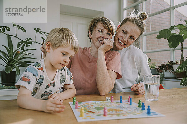 Mütter schauen zu  während ihr Sohn zu Hause ein Brettspiel spielt