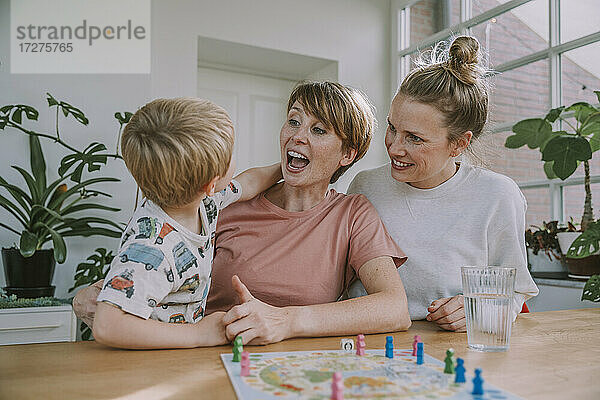 Fröhliche Mütter schauen zu  während ihr Sohn zu Hause ein Brettspiel spielt