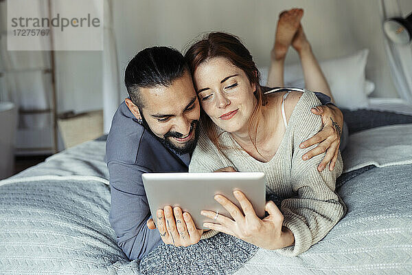 Mann  der eine Frau umarmt  während er ein digitales Tablet zu Hause benutzt