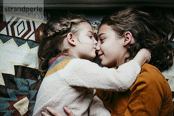Mädchen küsst Schwester  während sie zu Hause auf einer Decke liegt