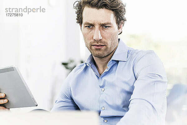 Mann konzentriert sich bei der Verwendung eines digitalen Tablets im Büro sitzend