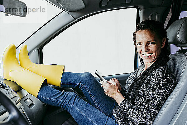 Lächelnde Frau mit Smartphone im Auto sitzend