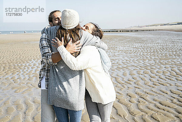 Junge Frau umarmt Mann und Mutter  während sie am Strand steht