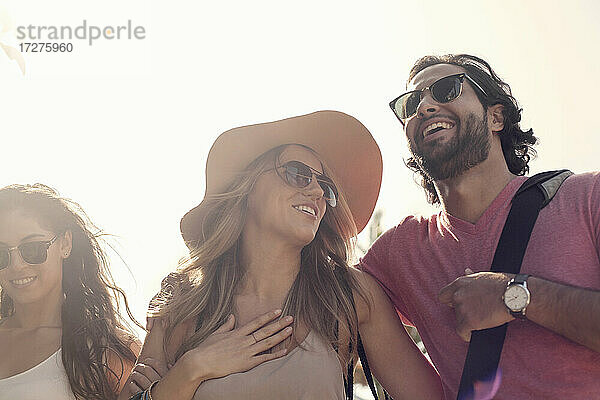 Lächelnde männliche und weibliche Freunde mit Sonnenbrillen im Gespräch gegen den klaren Himmel