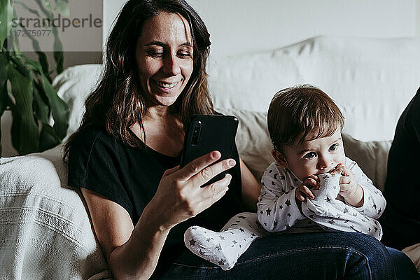 Mutter schreibt eine SMS auf ihrem Smartphone  während ihr Sohn zu Hause auf dem Sofa sitzt