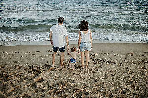 Mann und Frau mit Sohn betrachten die Aussicht  während sie bei Sonnenuntergang am Strand stehen