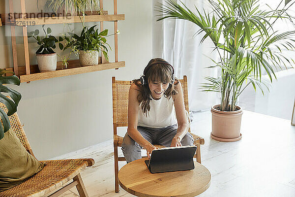 Lächelnde reife Frau  die ein digitales Tablet benutzt  während sie zu Hause sitzt