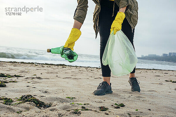 Umweltschützer mit Müllsack  der den Strand säubert  während er gegen den klaren Himmel steht