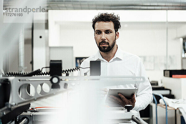 Männlicher Fachmann  der sich Maschinen ansieht  während er ein digitales Tablet in der Industrie hält