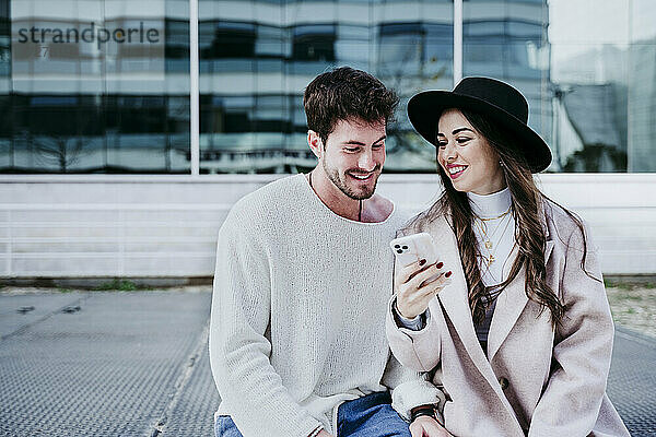 Lächelnde Frau zeigt ihrem männlichen Partner in der Stadt ihr Smartphone