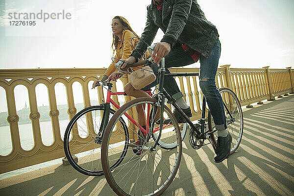 Heterosexuelles Paar fährt Fahrrad auf einer Brücke gegen den Himmel