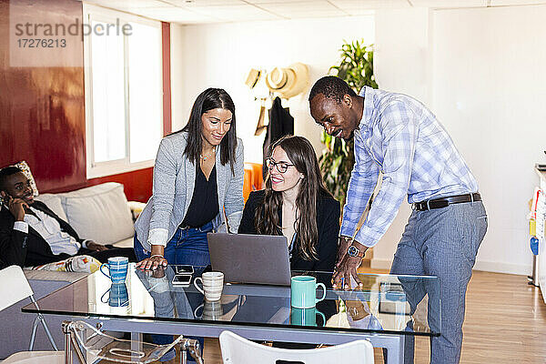Lächelnde männliche und weibliche Kollegen  die während einer Besprechung in einem Coworking-Büro über einen Laptop diskutieren