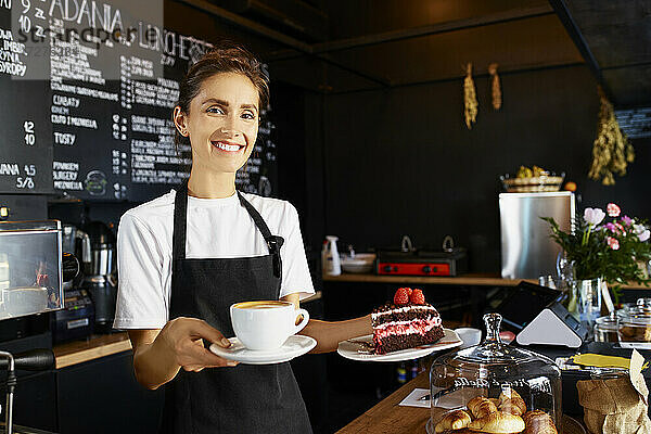 Porträt einer lächelnden Kellnerin  die Kaffee und Gebäck in einem Café serviert