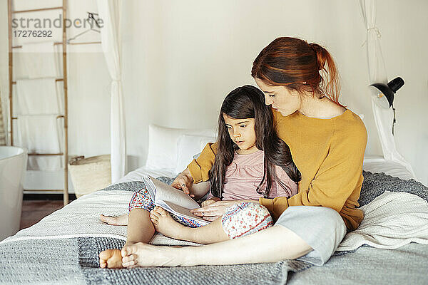 Mutter und Tochter lesen ein Buch  während sie zu Hause auf dem Bett sitzen