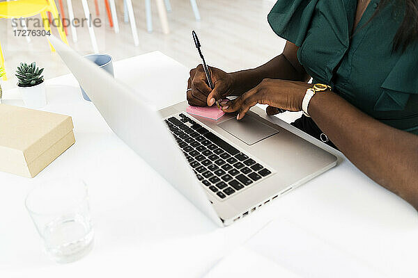 Geschäftsfrau schreibt auf Haftnotiz  während sie am Laptop im Büro arbeitet
