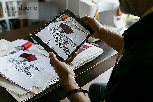Männlicher Schneider beim Fotografieren einer Skizze durch ein digitales Tablet im Arbeitsstudio