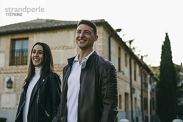 Lächelnder Freund und Freundin schauen weg  während sie auf der Straße in der Stadt spazieren gehen