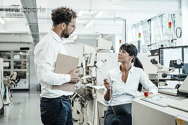 Selbstbewusste Technikerin im Gespräch mit einem männlichen Kollegen im Labor