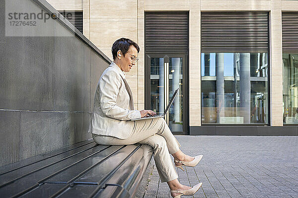 Frau benutzt Laptop  während sie auf einer Bank vor einem Gebäude sitzt