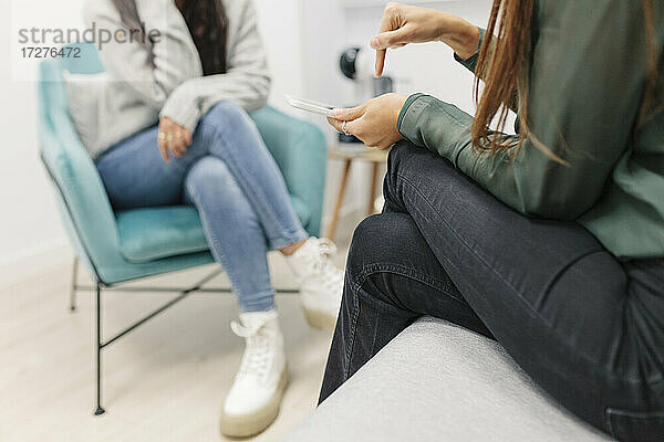 Weiblicher Psychologe  der auf ein digitales Tablet zeigt  während er mit einem Patienten im Büro sitzt