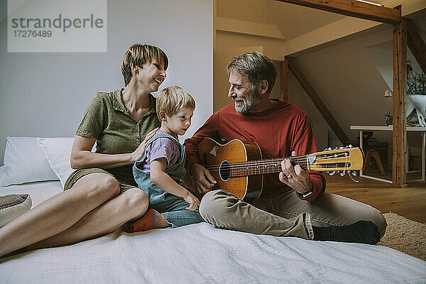 Vater spielt Gitarre  während Mutter und Sohn auf dem Bett im Schlafzimmer sitzen
