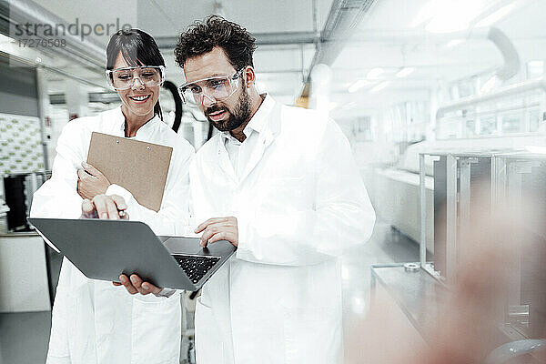 Lächelnde Wissenschaftlerin schaut auf einen männlichen Techniker  der einen Laptop im Labor benutzt
