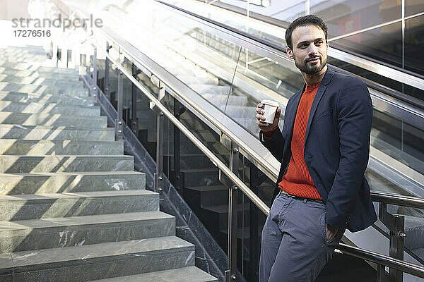 Selbstbewusster Unternehmer trinkt Kaffee  während er auf einer Treppe in der Stadt steht