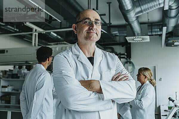 Selbstbewusster Wissenschaftler mit einem Mitarbeiter im Hintergrund im Labor stehend