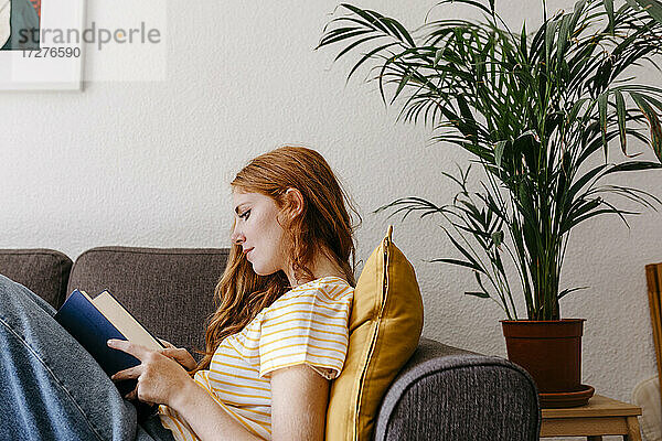 Junge Frau liest ein Buch  während sie zu Hause auf dem Sofa liegt