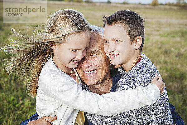 Lächelnder Großvater umarmt Enkelkinder auf dem Feld