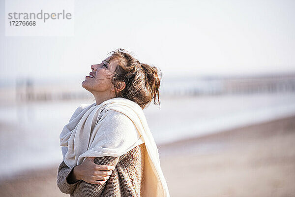 Lächelnde Frau mit verschränkten Armen und Blick auf den Strand an einem sonnigen Tag