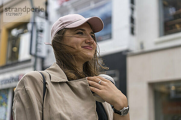 Junge Frau hält Einweg-Kaffeebecher  während sie auf der Straße in der Stadt steht