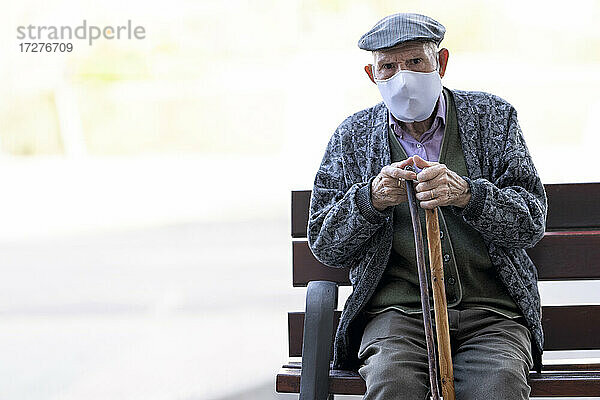 Älterer Mann mit Gesichtsschutzmaske sitzt auf einer Bank im Freien