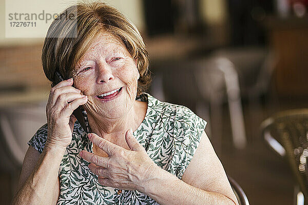 Glückliche Frau  die in einem Café sitzt und mit ihrem Handy telefoniert