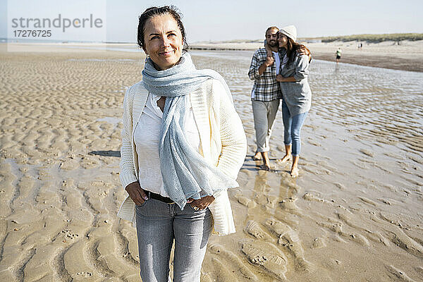 Reife Frau schaut weg  während sie mit einem Paar im Hintergrund am Strand steht