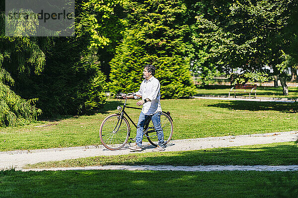 Älterer Mann schaut weg  während er mit dem Fahrrad in einem öffentlichen Park spazieren geht