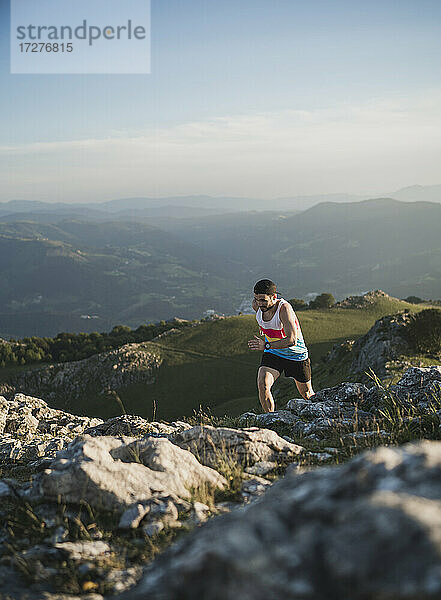 Mann läuft auf Bergpfad gegen Gebirge und klaren Himmel