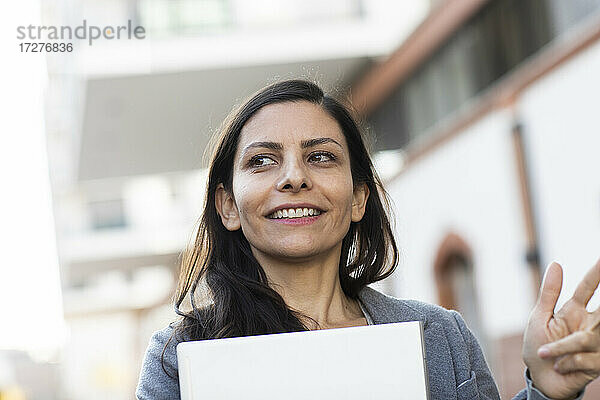 Geschäftsfrau  die einen Laptop hält und wegschaut  während sie vor einem Gebäude steht