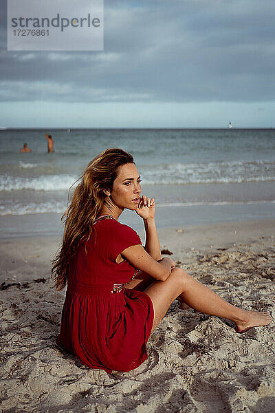 Nachdenkliche Frau  die wegschaut  während sie am Ufer des Strandes sitzt