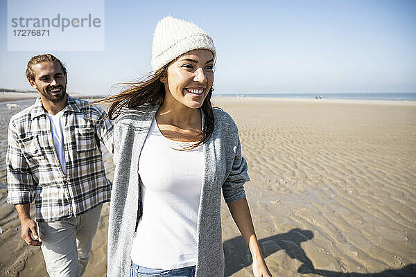Junge Frau hält die Hand eines Mannes beim Spaziergang am Strand