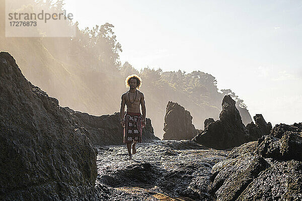 Junger Mann  der auf einer Felsformation am Strand gegen den Himmel läuft
