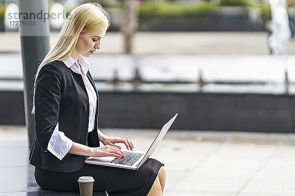 Blonde Geschäftsfrau arbeitet am Laptop  während sie auf einer Bank sitzt