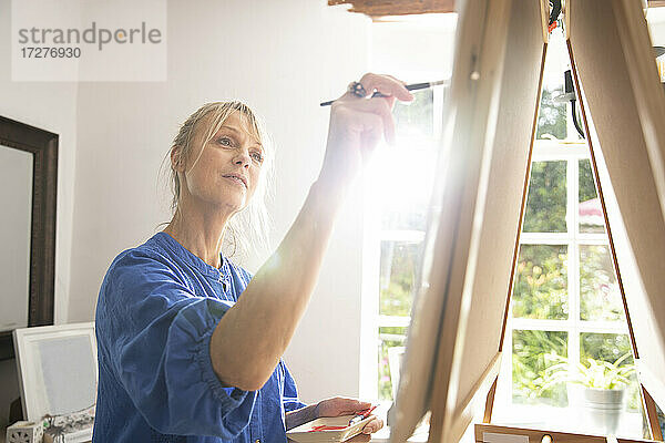 Ältere Frau konzentriert sich beim Malen auf der Staffelei zu Hause
