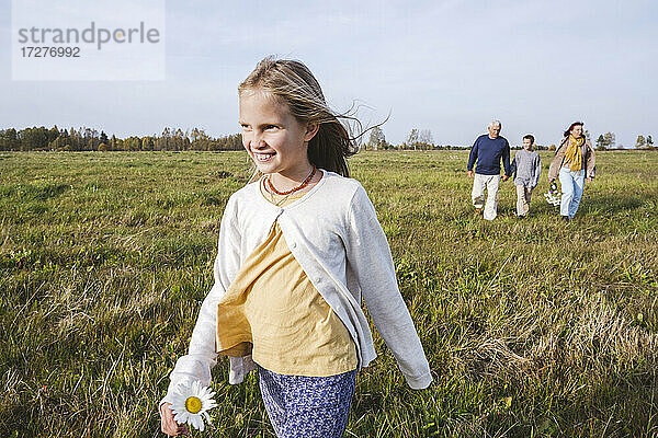 Lächelndes Mädchen  das auf einem Feld läuft  während die Familie im Hintergrund zu sehen ist