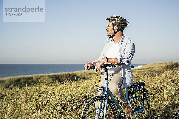 Mann betrachtet die Aussicht  während er auf einem Fahrrad auf einer Wiese vor einem klaren Himmel sitzt