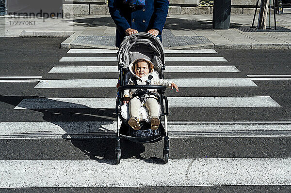 Vater mit Baby im Kinderwagen beim Überqueren der Straße in der Stadt