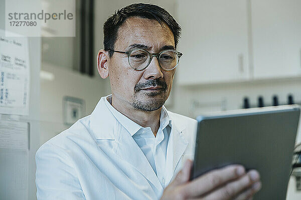 Wissenschaftler mit Brille  der im Labor stehend an einem digitalen Tablet arbeitet
