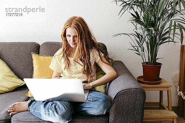 Junge Frau benutzt einen Laptop  während sie zu Hause auf dem Sofa sitzt