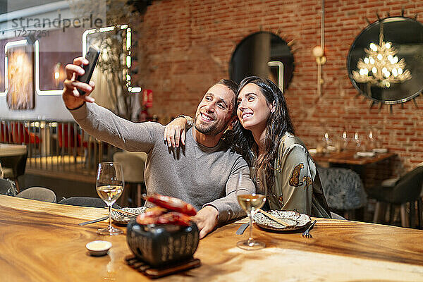 Lächelnde Freunde  die ein Selfie mit dem Handy machen  während sie am Tisch im Restaurant sitzen