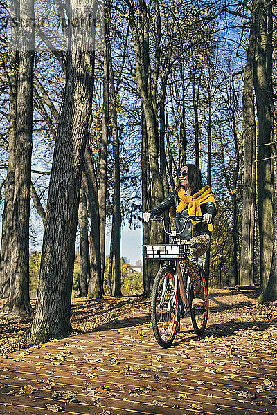 Glückliche Frau schaut weg  während sie an einem sonnigen Tag im Park Fahrrad fährt